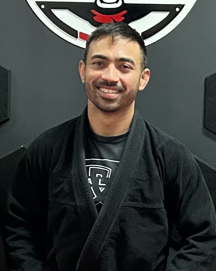 Chad Seng, head coach at Seng's Martial Arts, in a black gi in front of the Ape Jiu Jitsu crest.