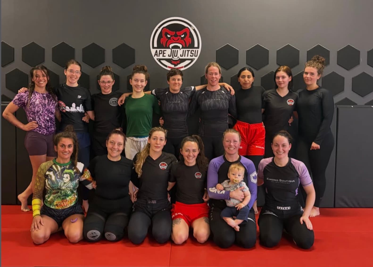 Fifteen women from Seng's gathered together on the mat under the Ape Jiu Jitsu crest, one of them holding a baby.
